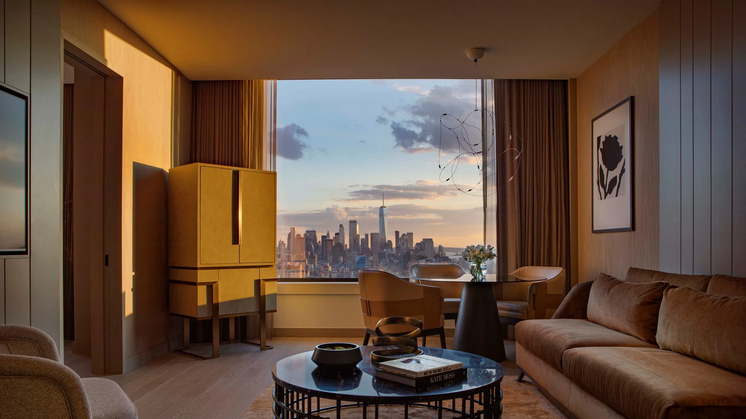 A hotel suite at golden hour, low sun across a velvet sofa and a round marble table, with the city skyline beyond a wide window.